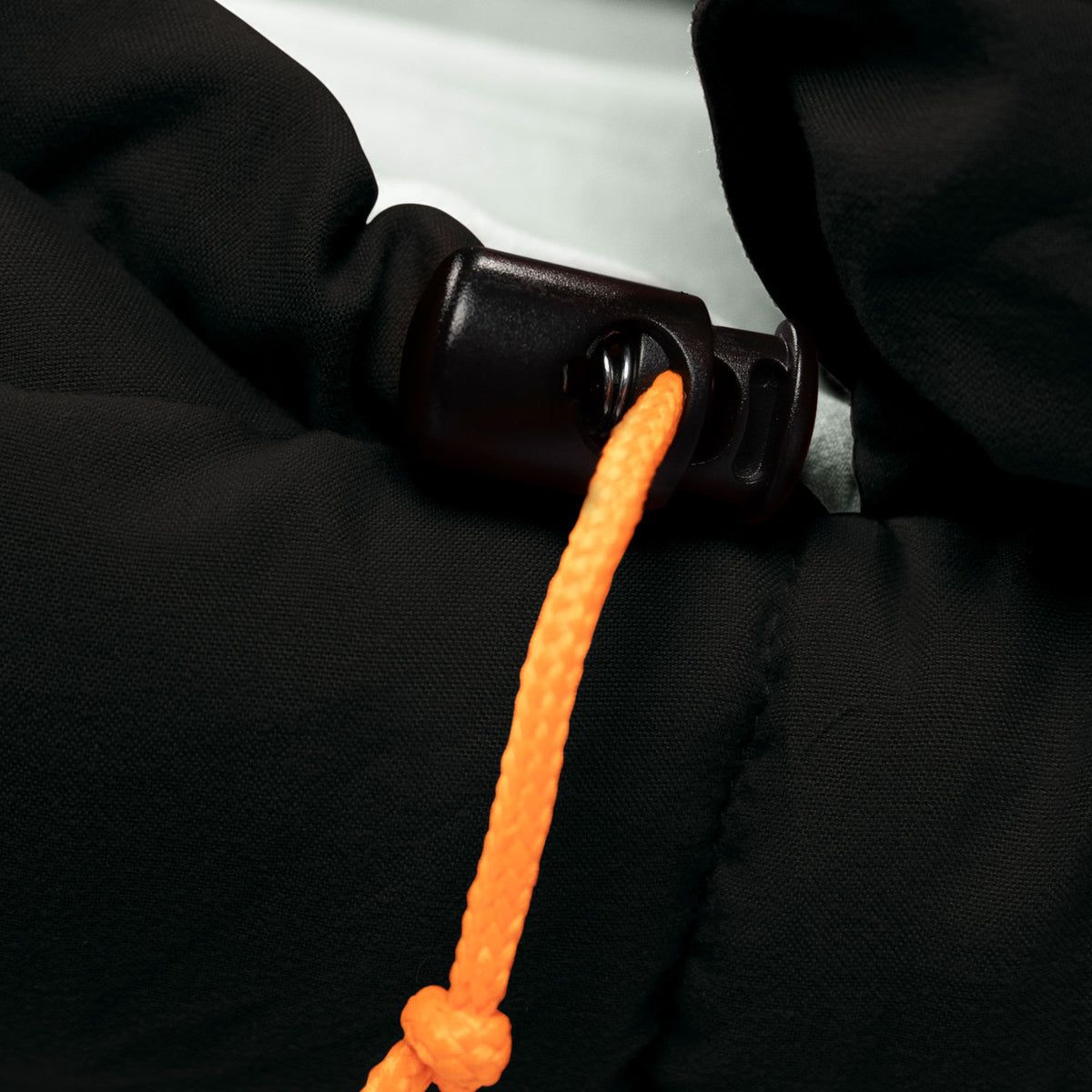 Close-up of a black carabiner with an orange rope tied around it on a black background.