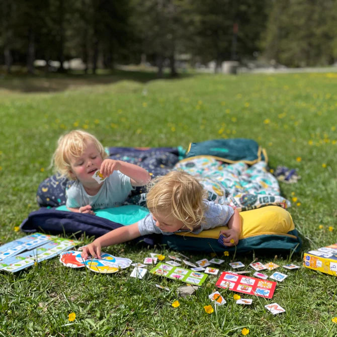 Two children in a field playing a card game whilst in their Toddler Bundle Beds Camping and Sleepover Beds, in Space and Adventure Designs. The best camping and sleepover toddler bed